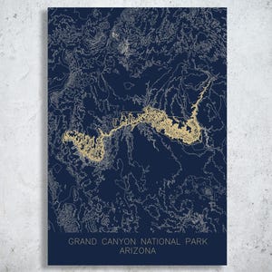 May include: A navy blue print of the Grand Canyon National Park in Arizona. The map features gold-colored contour lines and the park's outline. The text "GRAND CANYON NATIONAL PARK ARIZONA" is printed at the bottom of the print.