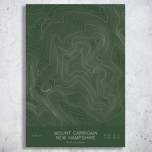 May include: A rectangular wall art print featuring a dark green background with white topographic contour lines. The text reads MOUNT CARRIGAIN NEW HAMPSHIRE, 4,700 ft., White Mountains, and the coordinates 44 05 37 N 71 26 48 W in white font.