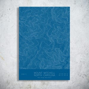 May include: A rectangular print featuring a blue background with white topographic contour lines of Mount Mitchell, North Carolina. The bottom section includes the text Mount Mitchell, North Carolina, Blue Ridge Mountains, 6,684 ft, and coordinates.