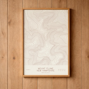 May include: A rectangular framed print featuring a topographic map of Mount Flume in New Hampshire with brown contour lines on a cream background. The text reads Mount Flume New Hampshire, 4,328 ft, and 44 06 32 N 71 37 41 W.