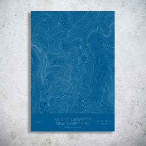 May include: A blue and white topographic map print of Mount Lafayette in New Hampshire. The map shows contour lines and includes the mountain's elevation, coordinates, and the text "White Mountains."