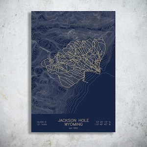 May include: A dark blue poster featuring a topographic map of Jackson Hole, Wyoming, with gold lines representing ski trails. The text reads Jackson Hole Wyoming, est 1965, 10,450 ft, 131 trails, and the coordinates 43 35 15 N 110 49 40 W.