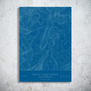 May include: A blue and white topographic map print of Mount Kosciuszko in Australia. The print includes the mountain's elevation of 2,228 meters and coordinates. The text "MOUNT KOSCIUSZKO AUSTRALIA" is displayed at the bottom.
