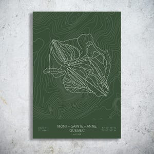 May include: A dark green rectangular print featuring a white topographic map of Mont-Sainte-Anne, Quebec. The design includes white contour lines, ski trail paths, and text stating 2,625 ft, 71 trails, and est 1966 at the bottom of the poster.