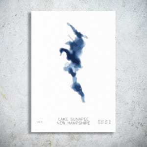 May include: A white rectangular print featuring a blue bathymetric map of Lake Sunapee, New Hampshire. The design displays layered shades of blue to indicate water depth, with the text Lake Sunapee New Hampshire, 100 ft, and coordinates 43 23 24 N 72 03 00 W.