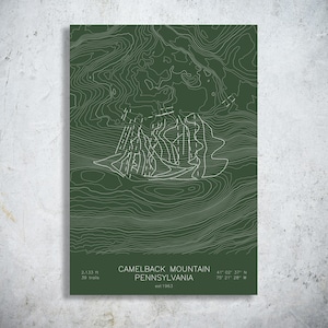 May include: A dark green topographic map print of Camelback Mountain, Pennsylvania. The design features white contour lines, ski trail markings, and text stating 2,133 ft, 39 trails, est 1963, and coordinates 41 02 37 N 75 21 26 W.