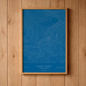 May include: A framed topographic map print of Nanga Parbat, Pakistan, in the Himalayas. The design features white contour lines on a deep blue background. Text at the bottom reads: 8,126 m, Nanga Parbat, Pakistan, Himalayas, 35 14' 16" N, 74 35' 21" E.