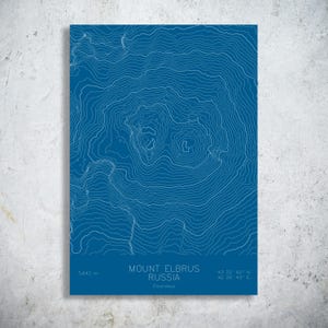 May include: A blue print of Mount Elbrus in Russia, featuring white topographic lines. The print includes the mountain's elevation of 5,642 m and coordinates. The text reads "Mount Elbrus Russia Caucasus".