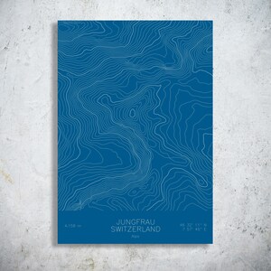 May include: A blue print of the Jungfrau mountain in Switzerland, with white contour lines. The poster includes the mountain's elevation, coordinates, and the word "Alps". The elevation is 4,158 m.