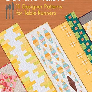 May include: The book cover features the title "Set the Table" with the subtitle "11 Designer Patterns for Table Runners." Various colorful table runner designs are displayed, showcasing patterns in yellow, white, blue, and green. The image includes a fork, spoon, and knife illustration.