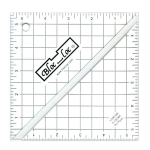 May include: A clear, square quilting ruler with black grid lines and measurements in inches. The ruler has a diagonal edge and the text "Bloc Loc" in a black rectangle. The website www.blocloc.com is also visible.