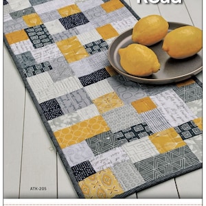 May include: A quilting pattern for a table runner called "Mini Brick Road" by Atkinson Designs. The pattern features a brick road design in shades of gray and yellow.
