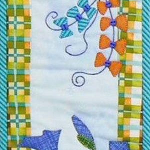 May include: A colorful, quilted wall hanging featuring a kite and morning glories. The kite is orange and yellow, with blue and orange bows. Blue morning glories and green leaves are below a black fence. The border is a mix of green, yellow, and blue.