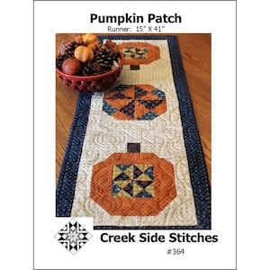 May include: Pumpkin Patch table runner with a blue and white border and three pumpkin designs. The runner is 15 inches by 41 inches. Creek Side Stitches #364.