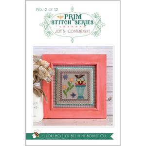 May include: A cross-stitch pattern titled Prim Stitch Series No. 2 of 12 Joy & Contentment by Lori Holt of Bee in My Bonnet Co. The design features a bird, flowers, and a geometric shape in a coral frame, displayed with a white vase of paper flowers.