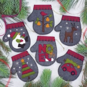May include: Set of ten felt Christmas ornaments shaped like mittens. Each mitten features a different festive design, including a snowman, a reindeer, a Christmas tree, a car, a pear tree, and the word "NOEL".