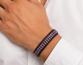 May include: A multi-strand bracelet featuring two rows of small, rectangular, light purple beads separated by silver-toned metal spacers, all set against a dark, textured black cord base that wraps around the wrist for a layered appearance.