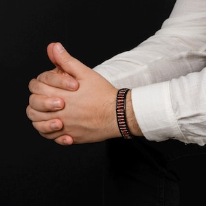 Op de afbeelding: Een zwarte leren armband met bruine en zilveren kralen.