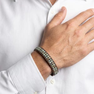 May include: A bracelet featuring two parallel rows of small, square, pale green beads held together by dark brown cord stitching. The beads have a smooth, matte finish and are arranged in a structured, linear pattern around the wrist.
