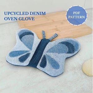 Peut inclure: Un gant de cuisine en denim recyclé en forme de papillon. Le gant de cuisine en denim bleu présente un motif patchwork avec des accents bleu foncé. Le texte "UPCYCLED DENIM OVEN GLOVE" est visible. Un cercle bleu avec le texte "PDF PATTERN" est également visible.