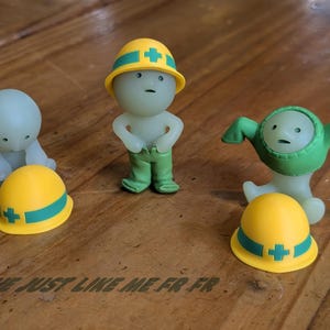 Puede incluir: Tres peque&ntilde;as figuras estilizadas. Una figura lleva un casco amarillo con una cruz verde y pantalones verdes. Otra figura lleva un traje verde. Una tercera figura est&aacute; arrodillada. El texto "ME JUST LIKE ME FR FR" est&aacute; en la parte inferior.