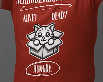 May include: Red t-shirt with a white graphic of a cat in a box. The text on the shirt reads "Schrödinger's Cat", "Alive?", "Dead?", and "Hungry."