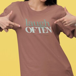 May include: A brown t-shirt with the text "laugh often" in white and green lettering.