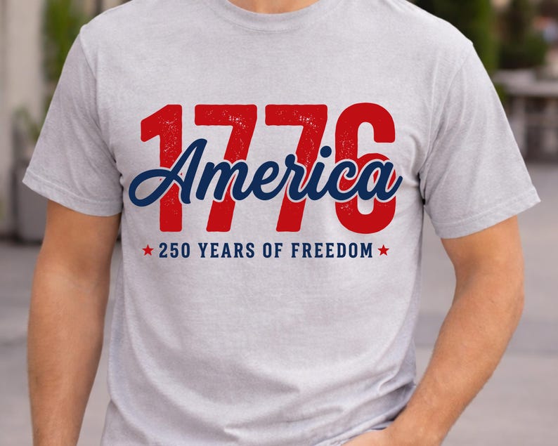 Pu&ograve; includere: T-shirt grigio chiaro con la scritta "1776 America" in rosso e blu. Sotto, c'&egrave; la scritta "250 YEARS OF FREEDOM" con stelle rosse. La maglietta &egrave; girocollo e ha maniche corte.