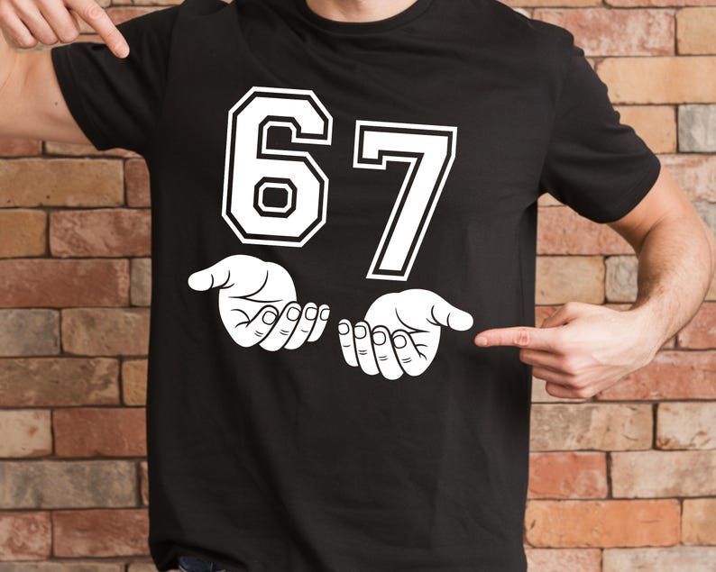 K&ouml;nnte beinhalten: Schwarzes T-Shirt mit der wei&szlig;en Zahl "67", schwarz umrandet. Darunter zwei wei&szlig;e H&auml;nde, Handfl&auml;chen nach oben. Das T-Shirt wird von zwei H&auml;nden gezeigt.