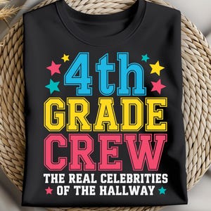 以下が含まれることがあります： 黒いTシャツ。青、黄、ピンクで「4th GRADE CREW」の文字と星のアクセント。 「THE REAL CELEBRITIES OF THE HALLWAY」のフレーズが下に印刷されています。 シャツは織られた円形の表面に表示されています。