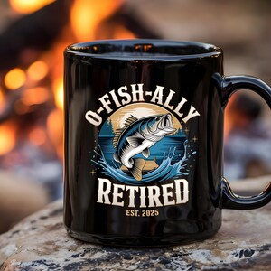 Puede incluir: Taza de caf&eacute; negra con un gr&aacute;fico de un pez saltando fuera del agua. El texto en la taza dice "O-Fish-Ally Retired Est. 2025".