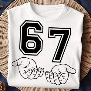 Pode incluir: Camisola branca com o n&uacute;mero 67 em letras pretas. Abaixo dos n&uacute;meros est&atilde;o duas m&atilde;os abertas em estilo de desenho linear. A camisola est&aacute; sobre uma superf&iacute;cie de vime tecido.