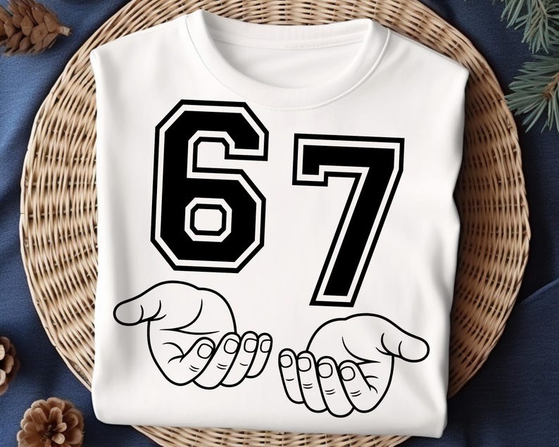 Pode incluir: Camisola branca com o n&uacute;mero 67 em letras pretas. Abaixo dos n&uacute;meros est&atilde;o duas m&atilde;os abertas em estilo de desenho linear. A camisola est&aacute; sobre uma superf&iacute;cie de vime tecido.