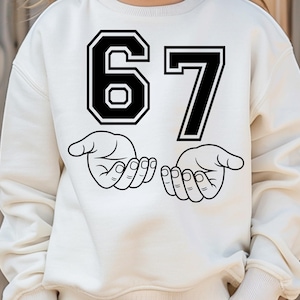 Pode incluir: Camisola creme com um gr&aacute;fico preto do n&uacute;mero 67 e duas m&atilde;os abertas. O n&uacute;mero 6 est&aacute; em estilo bloco e o n&uacute;mero 7 em uma fonte padr&atilde;o. As m&atilde;os s&atilde;o desenhadas em um estilo de arte de linha simples.