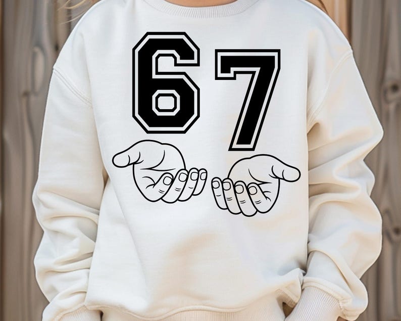 Pode incluir: Camisola creme com um gr&aacute;fico preto do n&uacute;mero 67 e duas m&atilde;os abertas. O n&uacute;mero 6 est&aacute; em estilo bloco e o n&uacute;mero 7 em uma fonte padr&atilde;o. As m&atilde;os s&atilde;o desenhadas em um estilo de arte de linha simples.