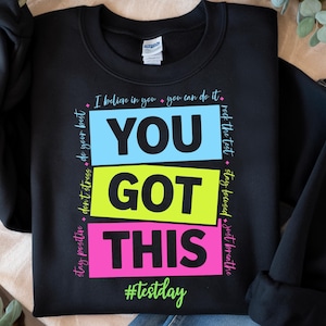 May include: Black sweatshirt with a motivational message in colorful blocks that reads "You Got This" with the hashtag "#testday" printed below. The text around the blocks reads "stay positive, don't stress, do your best, I believe in you, you can do it, rock the test, stay focused, just breathe."
