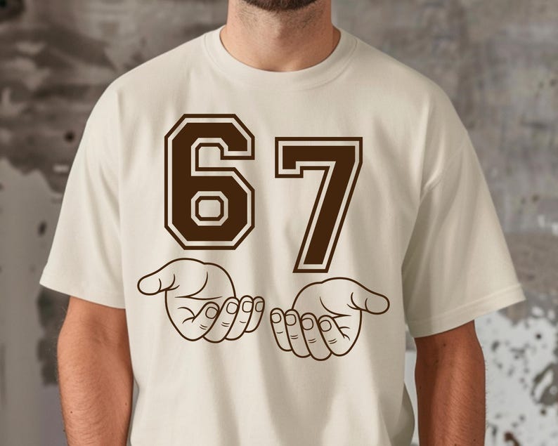 Pode incluir: Camiseta creme com o n&uacute;mero "67" em marrom, com contorno. Abaixo, duas m&atilde;os abertas em estilo de desenho linear. A camiseta &eacute; uma pe&ccedil;a casual e unissex.