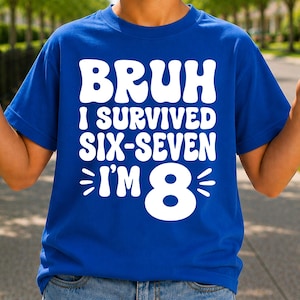 Könnte beinhalten: Ein königsblaues Kurzarm-T-Shirt mit fettgedrucktem weißem Text, der BRUH I SURVIVED SIX-SEVEN I'M 8 lautet. Die Grafik ist mittig auf der Brust platziert und enthält kleine dekorative Linien, die die große Zahl 8 am unteren Rand des Designs flankieren.