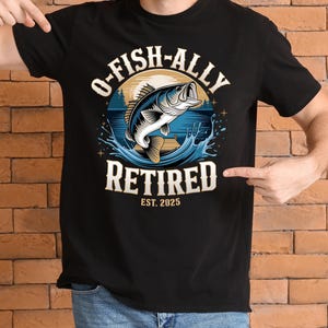 Puede incluir: Camiseta negra con un gr&aacute;fico de un pez saltando fuera del agua. El texto "O-Fish-Ally Retired Est. 2025" est&aacute; impreso en la camiseta.