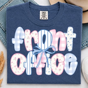 Könnte beinhalten: Ein marineblaues T-Shirt mit dem Schriftzug "front office" in großen, abgerundeten Buchstaben. Jeder Buchstabe zeigt ein anderes Muster, darunter hellblaues Vichy-Karo, rosa Blumen und blaue Streifen. Eine hellblaue Schleife ist mittig gebunden.