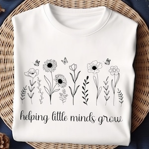 May include: White t-shirt with a black graphic of flowers and butterflies. The text "helping little minds grow" is printed below the graphic.