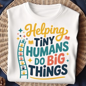 May include: White sweatshirt with the text "Helping Tiny Humans Do Big Things" in yellow, teal, orange, and navy blue. A ladder with handprints and stars is on the left side. The sweatshirt is on a woven surface.