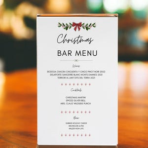 May include: A white Christmas bar menu with red holly and a red bow at the top. The menu lists wines, cocktails, and beers. The text reads "Christmas Bar Menu".