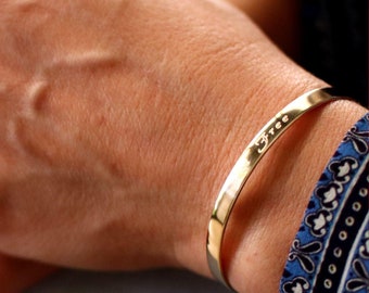 Puede incluir: Un brazalete de oro con la palabra "free" grabada.
