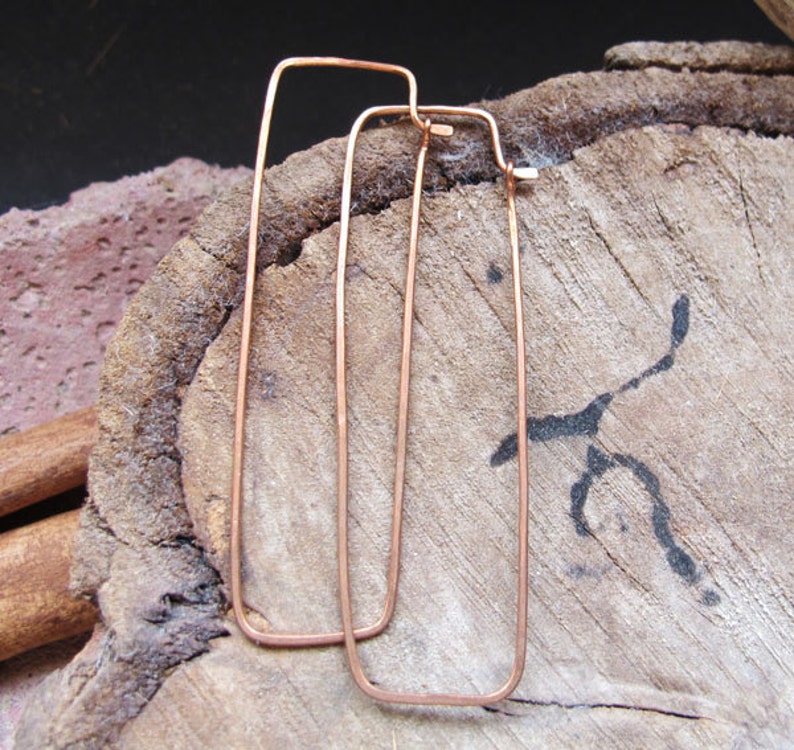 Puede incluir: Un par de pendientes de aro rectangulares de cobre. Los pendientes son simples y de dise&ntilde;o moderno.