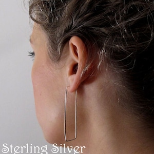 Puede incluir: Pendientes de aro geom&eacute;tricos de plata de ley. Los pendientes son de forma rectangular y se muestran en la oreja de una persona.
