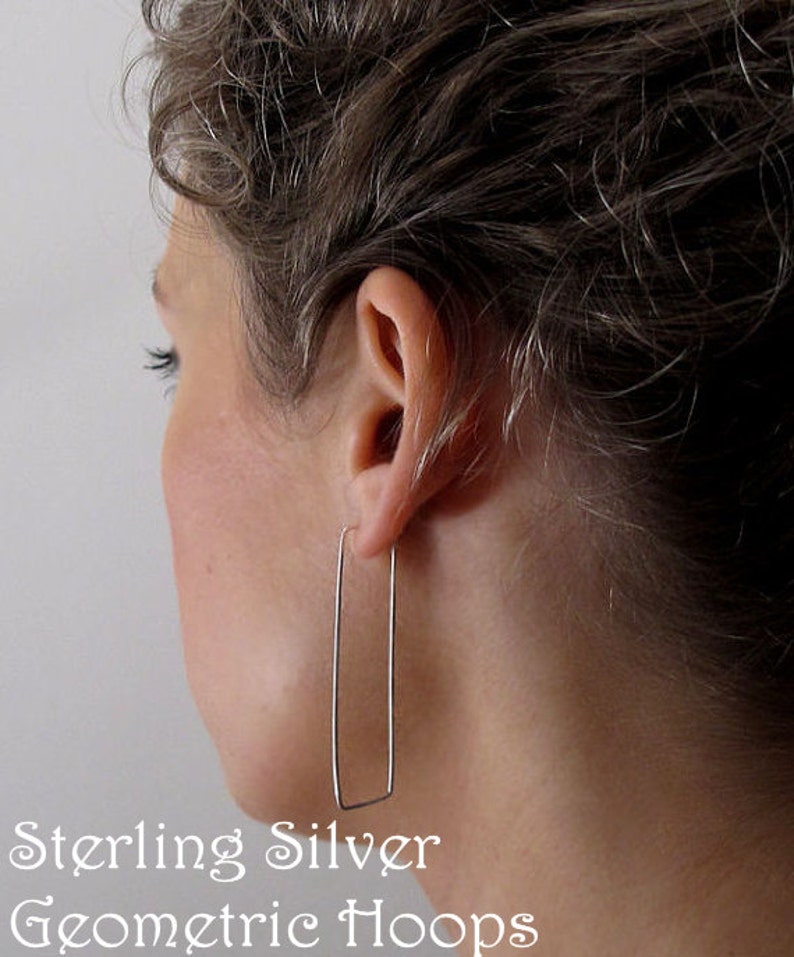 Puede incluir: Pendientes de aro geom&eacute;tricos de plata de ley. Los pendientes son de forma rectangular y se muestran en la oreja de una persona.