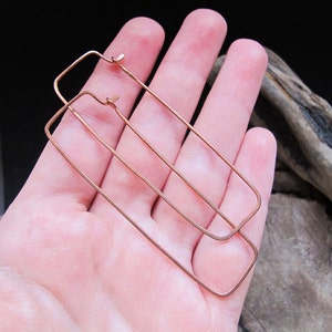 Puede incluir: Un par de pendientes de aro rectangulares de oro rosa. Los pendientes est&aacute;n hechos de alambre fino y miden aproximadamente 5 cm de largo.