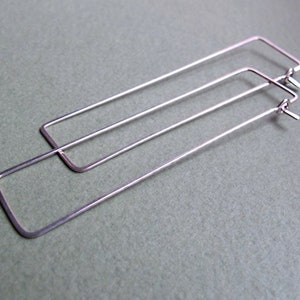 Puede incluir: Un par de pendientes de aro rectangulares de plata. Los pendientes est&aacute;n hechos de metal fino y tienen un dise&ntilde;o simple y moderno.