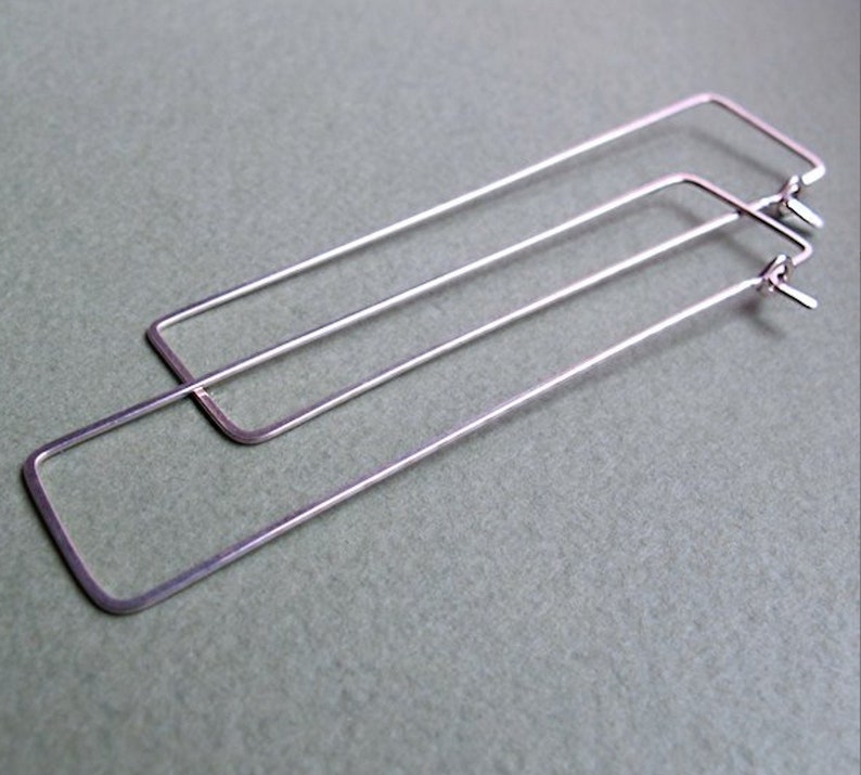 Puede incluir: Un par de pendientes de aro rectangulares de plata. Los pendientes est&aacute;n hechos de metal fino y tienen un dise&ntilde;o simple y moderno.